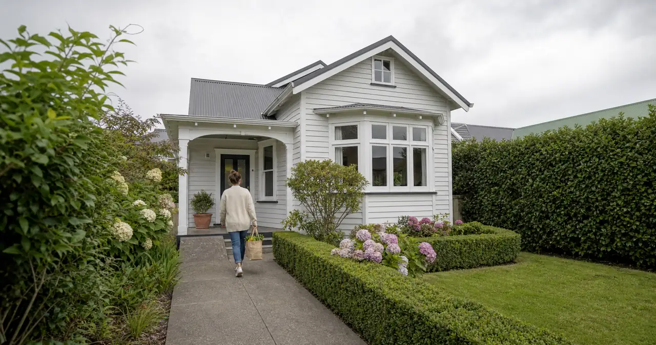 Buying your first home in New Zealand, on a weatherboard bungalow with a person walking up the front path.