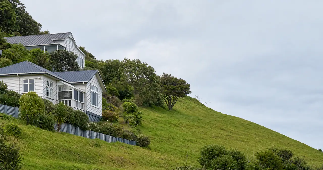 The Natural Hazards Commission explained, on weatherboard houses stepping up a steep hillside with retaining walls.