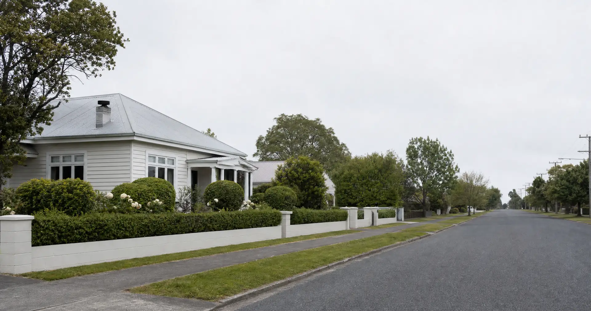 A quiet suburban street of single-storey weatherboard homes with iron roofs and low front hedges.